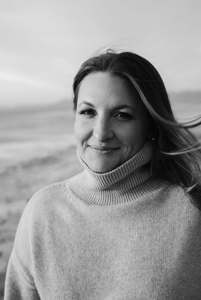 A woman standing at the great salt lake in a no color photo, smiling at the camera up close. 